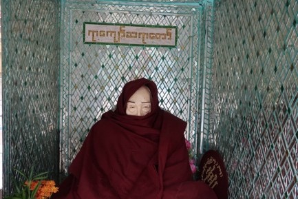 Monk with face covered inside an alcove with tiled walls.