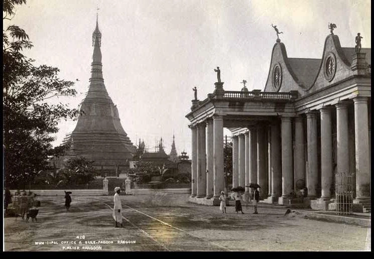 A black and white photograph of a colonial office building and a traditional pagoda in Yangon, formerly 'Rangoon'.
